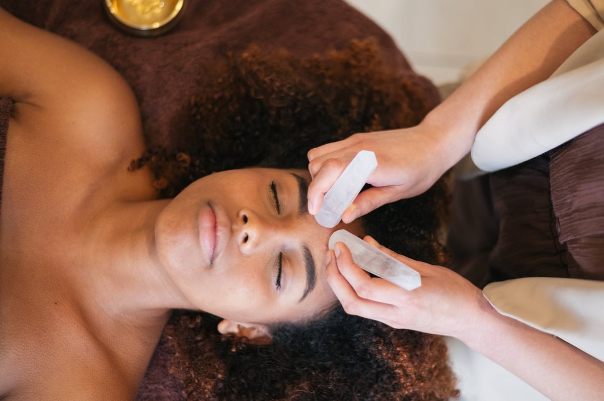 Woman enjoying a relaxing facial treatment with clear crystal wands on her forehead