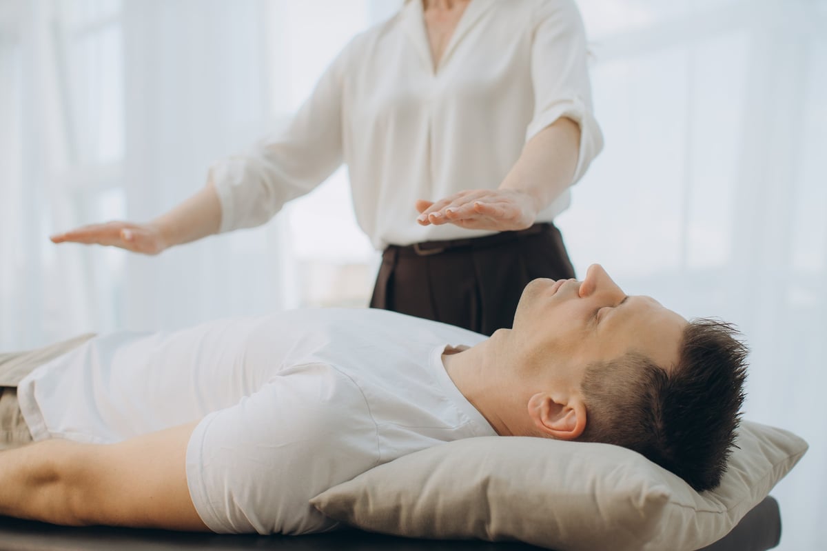 Woman healer performing theta healing or psychotherapist session on a man lying down, focusing on energy and mind wellness